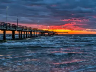 Sunrise at the Bob Hall Pier near Corpus Christi with clouds reflecting the orange lights of the sun. Turbulent sea.
