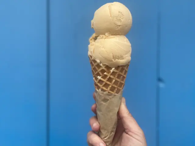 A hand holding a ice cream in a cone in front of a blue wall