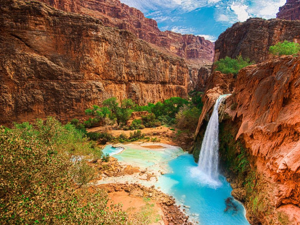 Grand Canyon, Arizona with Havasu Falls, waterfalls into a beautiful blue pool below and large mountains surrounding it.