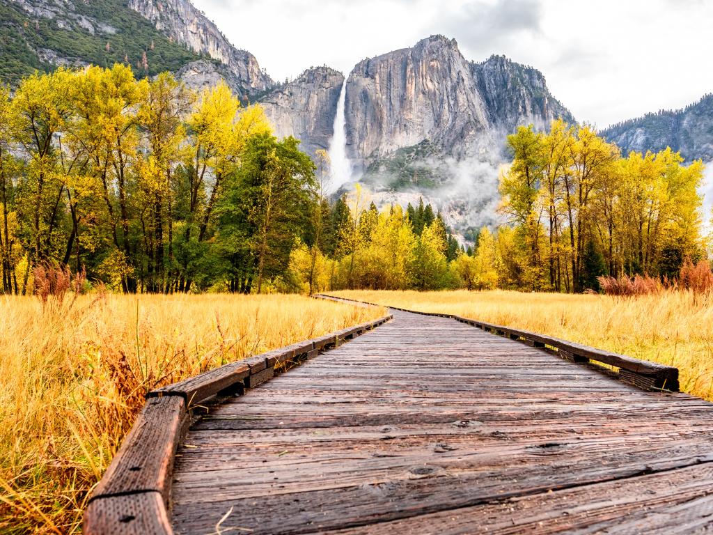 Meadow with boardwalk in Yosemite National Park Valley with Yosemite Falls at cloudy autumn morning. Low clouds lay in the valley. California, USA.