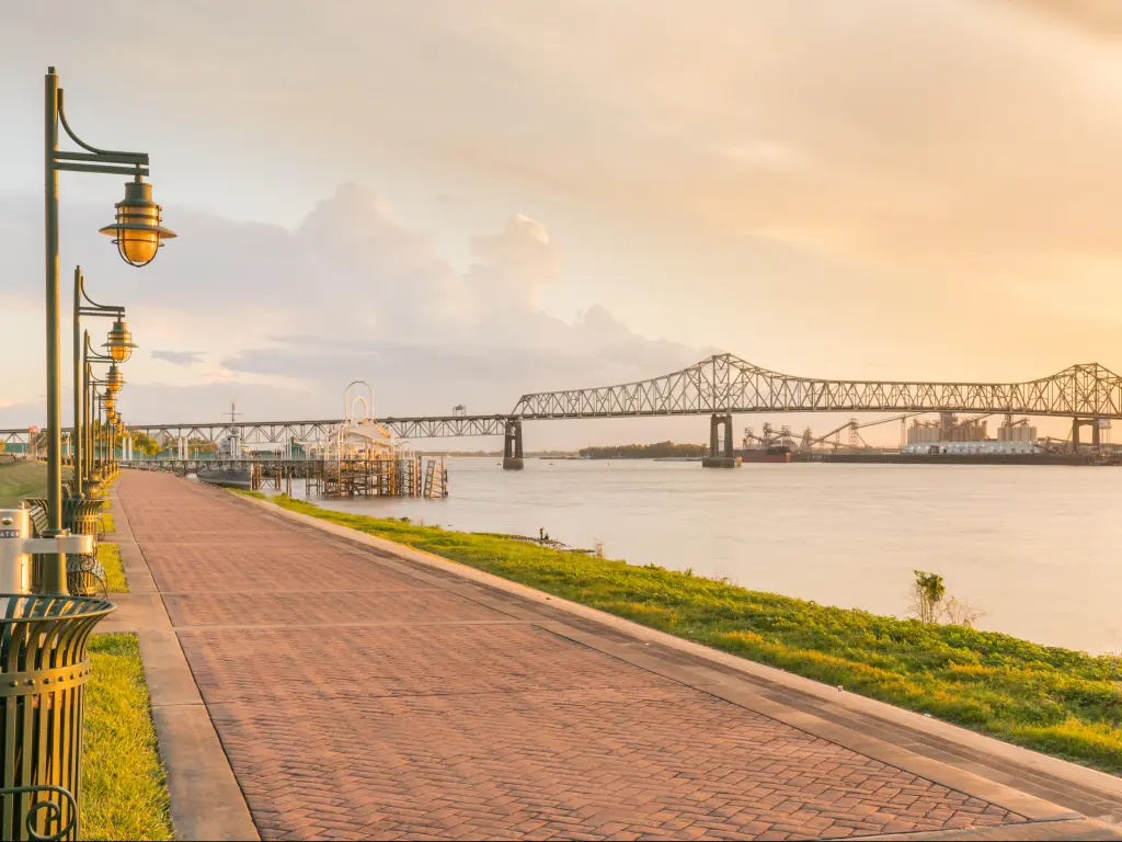 Baton Rouge, Louisiana with a path alongside the Mississippi River, street lamps to one side and an evening glow and the bridge in the background.