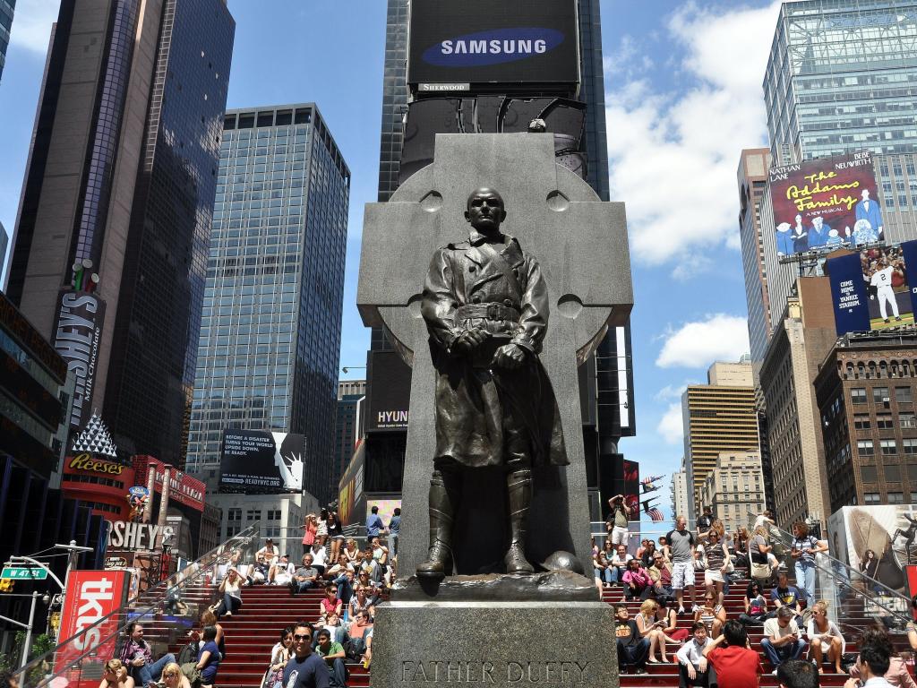 Close up of Statue of Father Duffy at Times Square, with skyscrapers and tourists in background