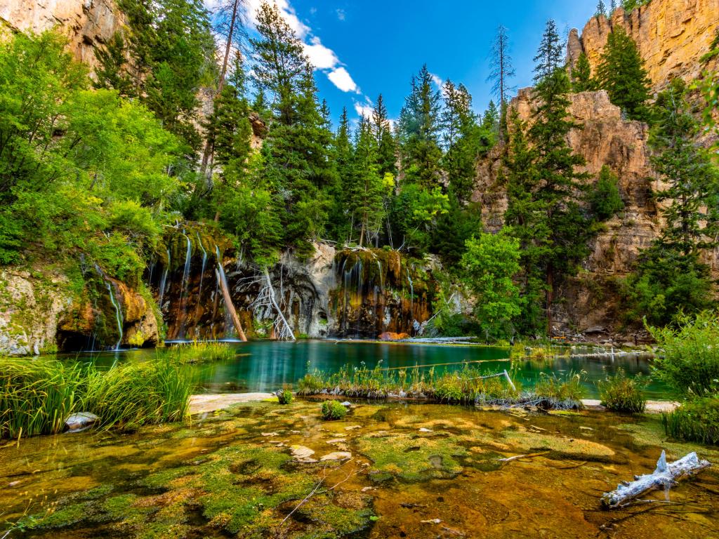 Glenwood Springs, Colorado, USA with a stunning image of Hanging Lake with mountains and trees surrounding the lake and taken on a sunny day.