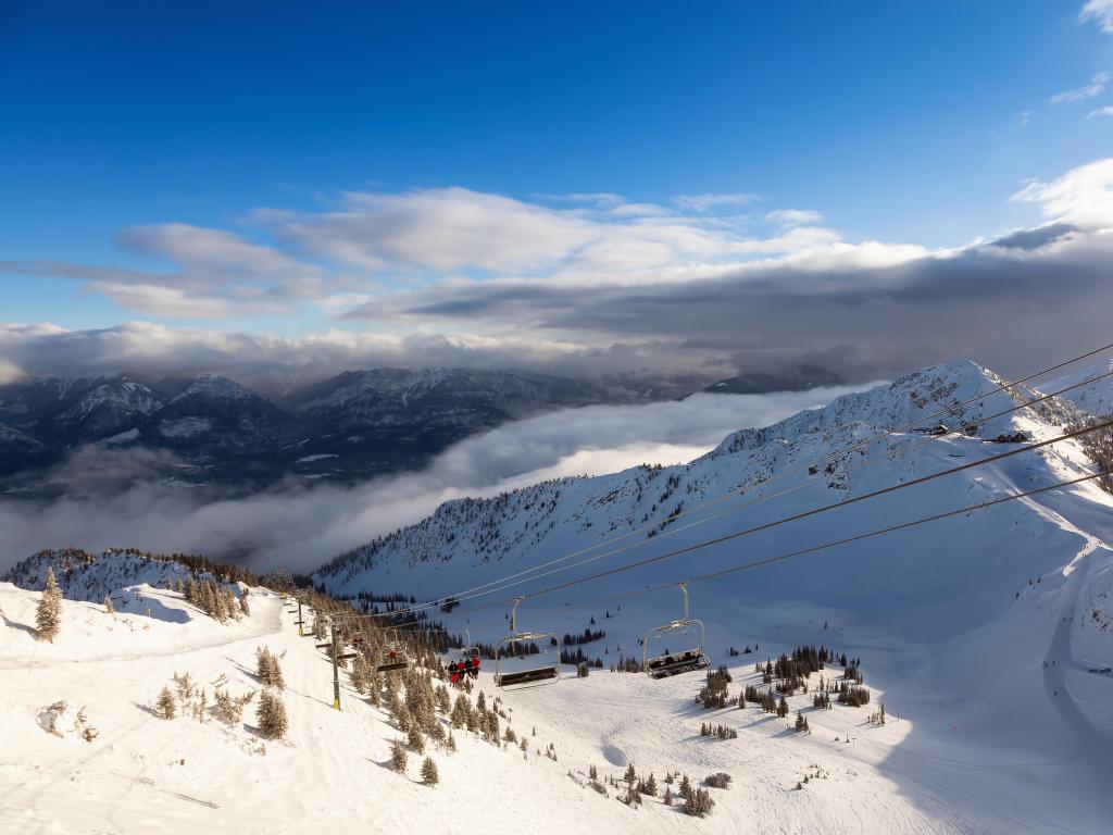 Chairlift going up a beautiful Canadian mountain during a vibrant sunny and cloudy morning sunrise in winter.