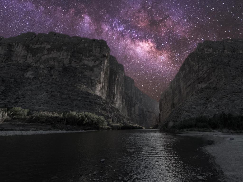 High cliffs with big river at the bottom, at night, with many stars in the night sky