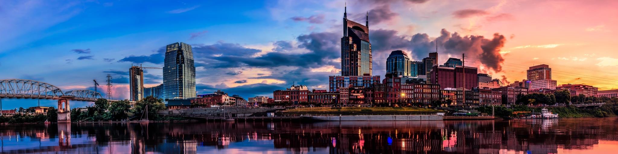 Nashville, TN, USA with the city skyline in the background and reflecting in the river in the foreground, taken at early evening with a dramatic sky.