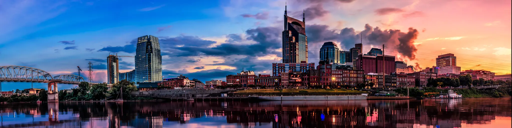 Nashville, TN, USA with the city skyline in the background and reflecting in the river in the foreground, taken at early evening with a dramatic sky.
