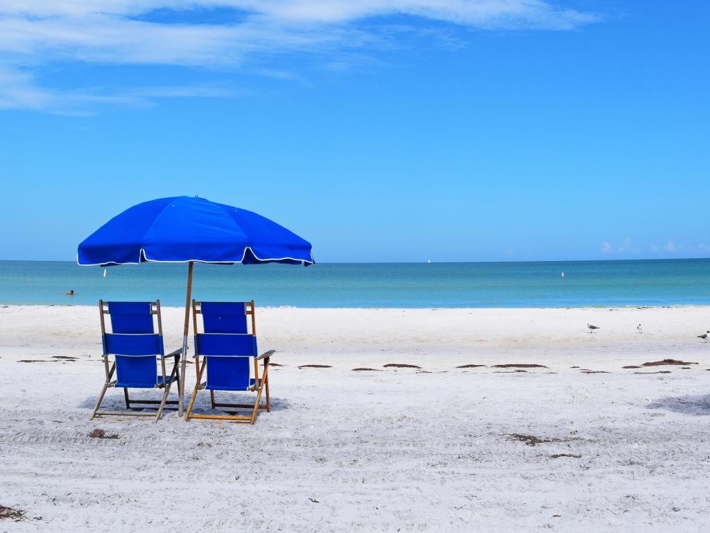 Brilliant blue umbrellas against white clouds and blue sky on the beach of Caladesi Island in Dunedin, Florida. Sand and seagrass, no people.