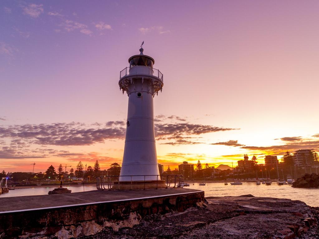 White lighthouse in front of harbour illuminated by golden sunset light