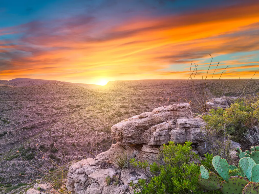 A beautiful, orange sunset over the hills of the Carlsbad Caverns National Park, rugged terrain ahead.