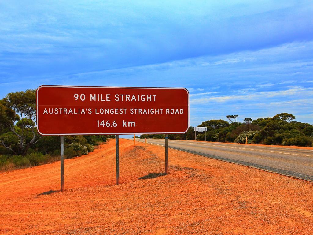 Red road sign next to grey road with orange dirt verges