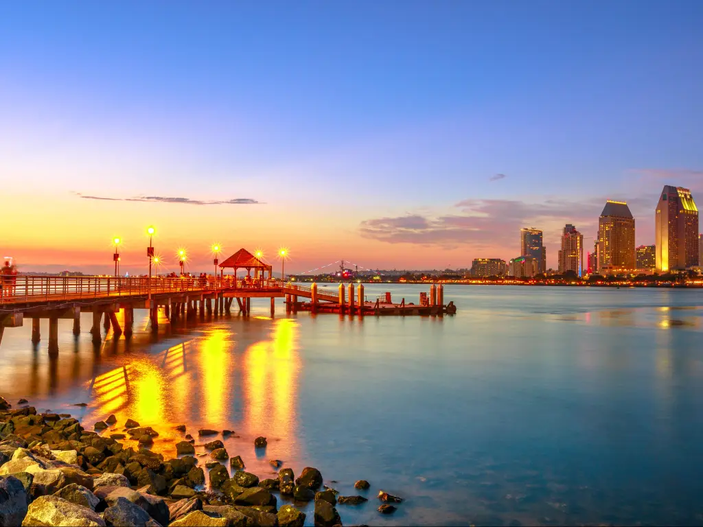 Scenic view of Coronado Ferry Landing on Coronado Island, California, USA. Downtown of San Diego at twilight on background. Old wooden pier reflecting on beach shore in San Diego Bay.