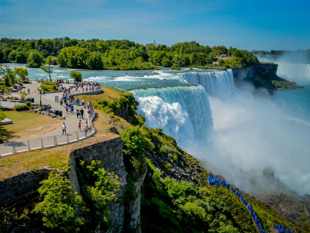 Water rushing down Niagara Falls with people looking down from the lookout above.