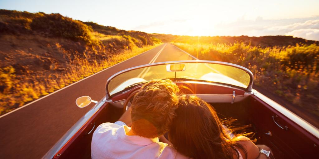 A couple driving down a road at sunset with his arm around her shoulder