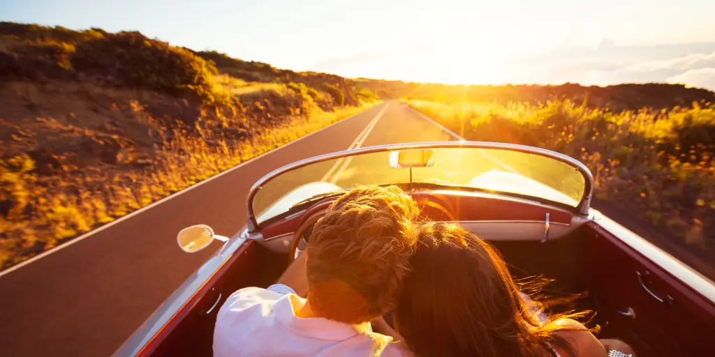 A couple driving down a road at sunset with his arm around her shoulder