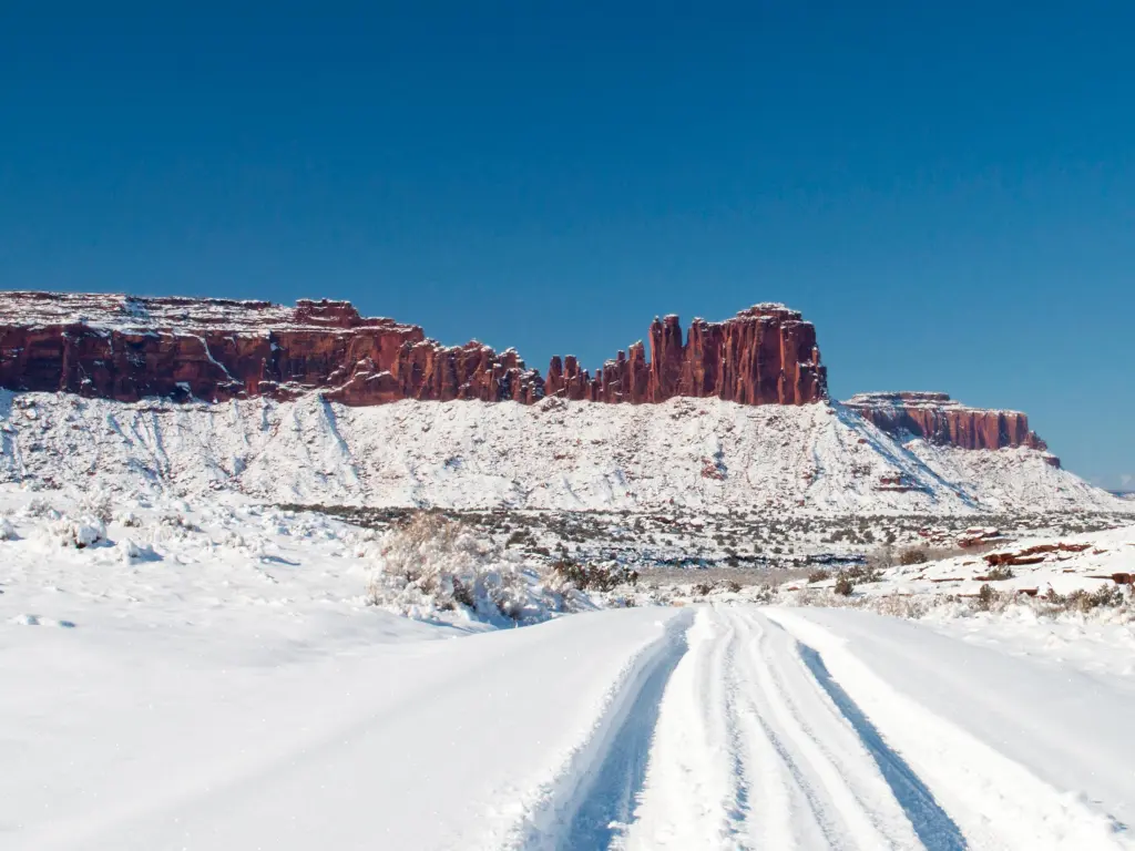 Red rock ridge with tire tracks in snow leading to it, near Canyonlands National Park, USA