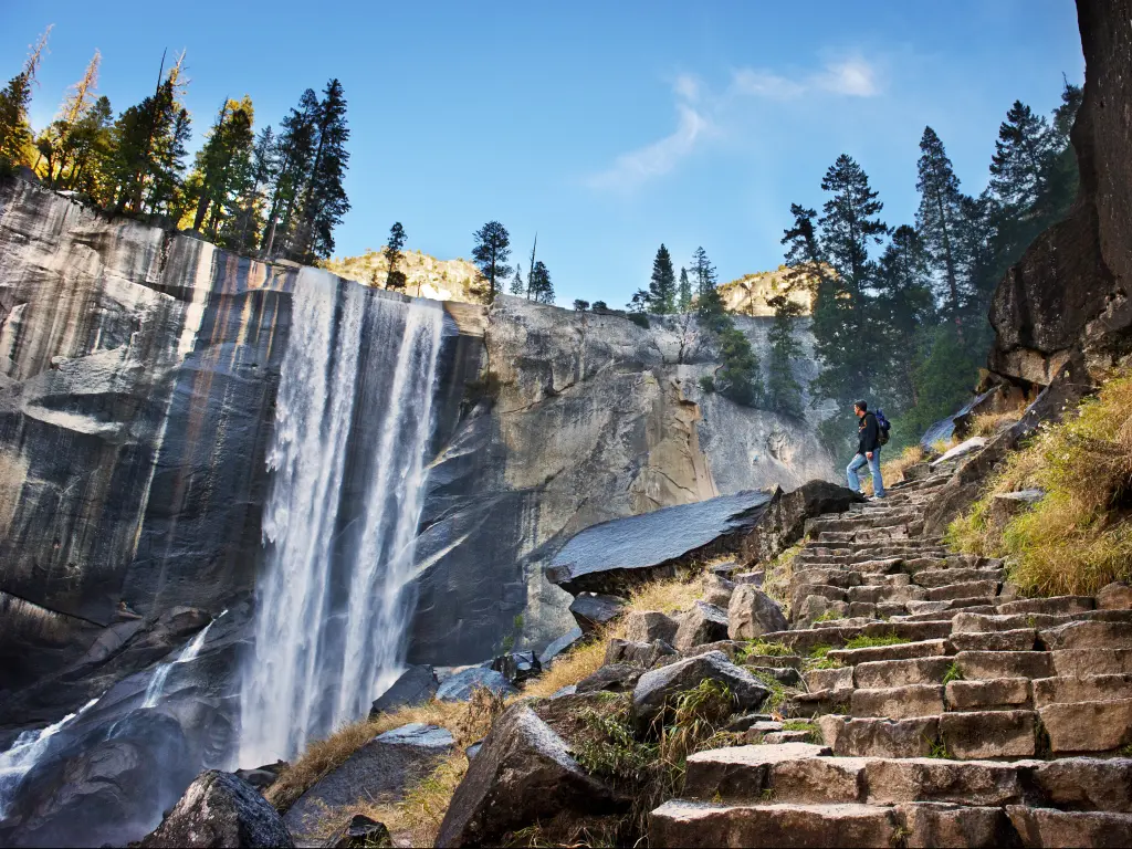A man at the top of the rock stairs indulges the scenic beauty of the waterfalls in Yosemite National Park. 