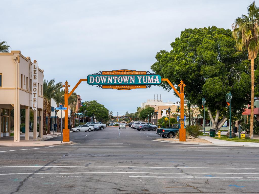 Orange and blue sign welcoming people to Downtown Yuma, Arizona, with retro fronted buildings and palm trees
