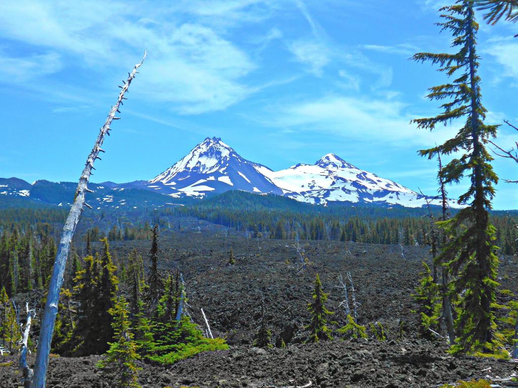 View of the North and Middle Sisters peaks from across the lava bed at McKenzie Pass, Oregon, with blue sky above