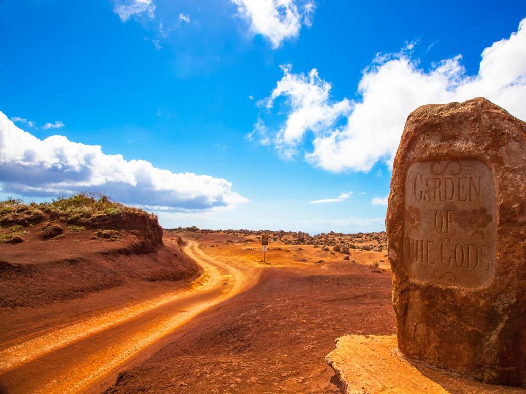 Red ground and dirt track running past a boulder sign for the Garden of the Gods in Lanai, Hawaii