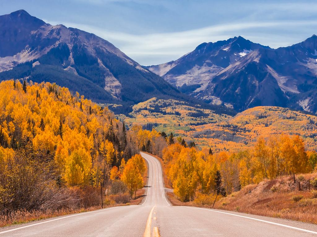 An empty Highway 45 road near Telluride, Colorado with trees during fall and a sight of mountains ahead.