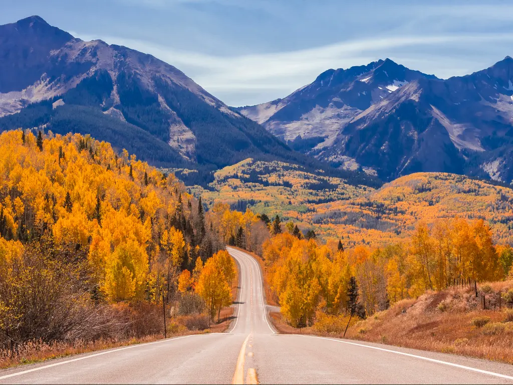 An empty Highway 45 road near Telluride, Colorado with trees during fall and a sight of mountains ahead.