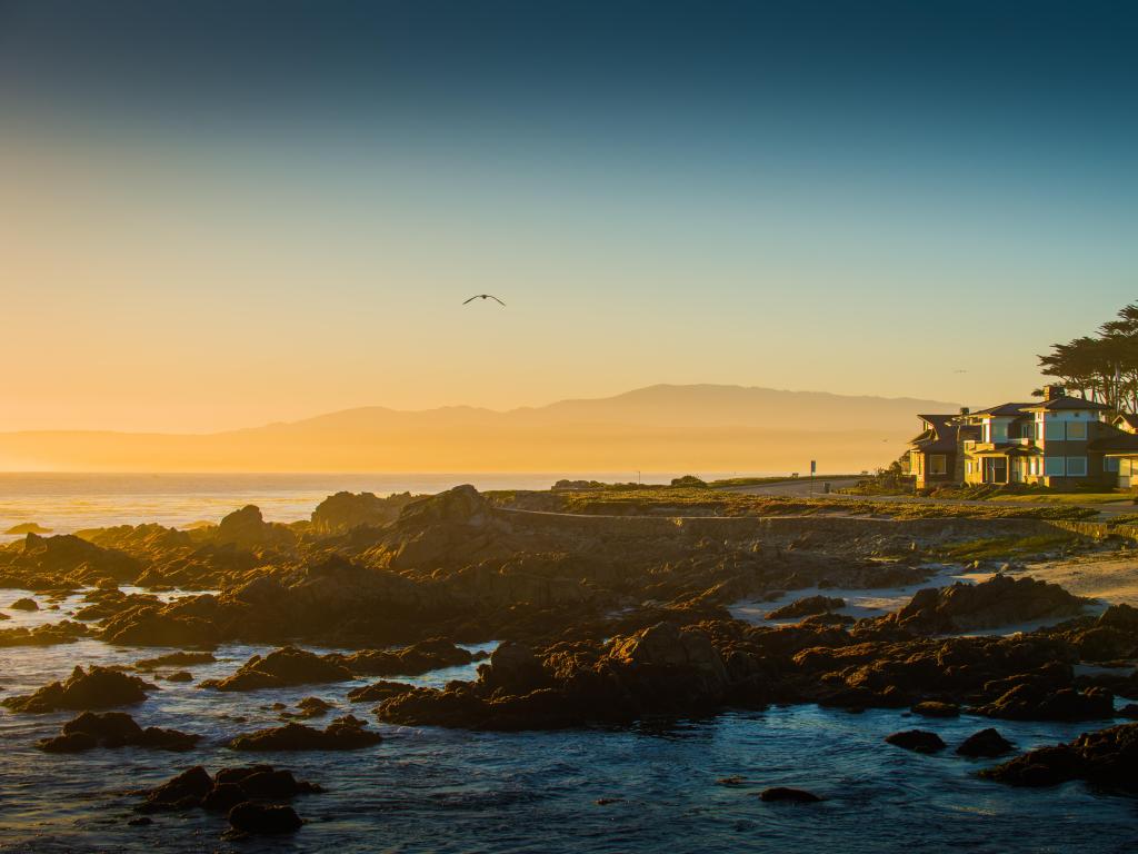 Sun sets behind a rocky shore with a house