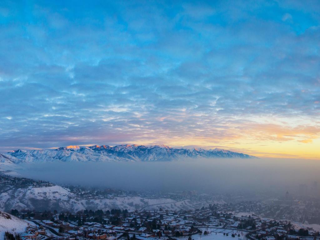 Salt Lake City at sunset with smog covering the lake and snow capped mountains in the foreground and background. 