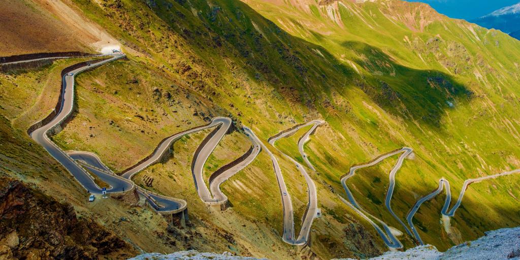 Aerial view of the Stelvio Pass road in the Italian Alps. It is a twisting road on a green mountain.