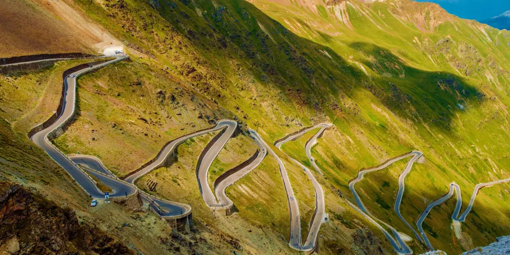 Aerial view of the Stelvio Pass road in the Italian Alps. It is a twisting road on a green mountain.