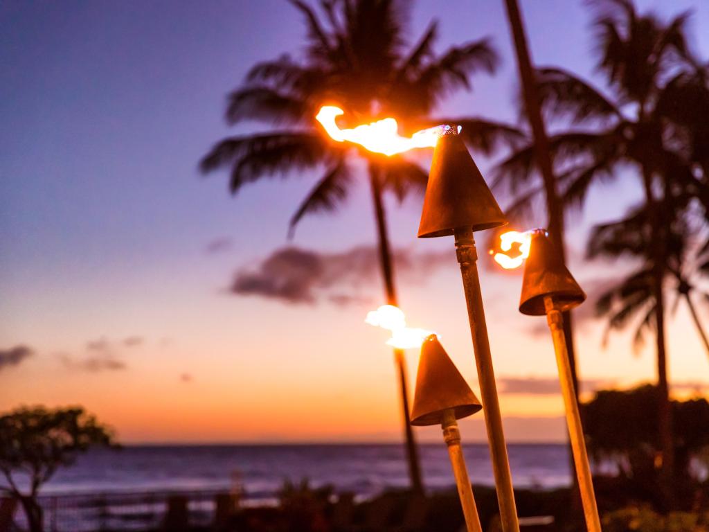 Close up shot of fire torches burn at sunset at a Luau in Hawaii, with flames dancing in the breeze