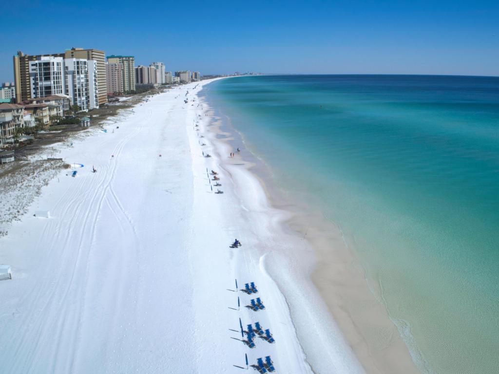 Blue waters of the Gulf of Mexico and white sands of Destin meet, with hotels and buildings in the background.