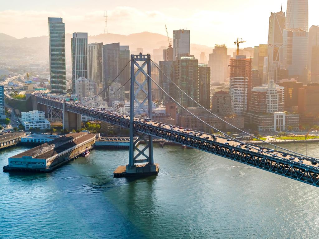 San Francisco, California, USA with an aerial view of the Bay Bridge in the foreground and city skyline in the distance on a foggy sunrise. 