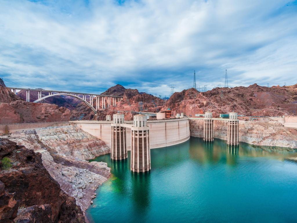 Turquoise lake with bare rocks either side and Hoover dam and bridge cutting across