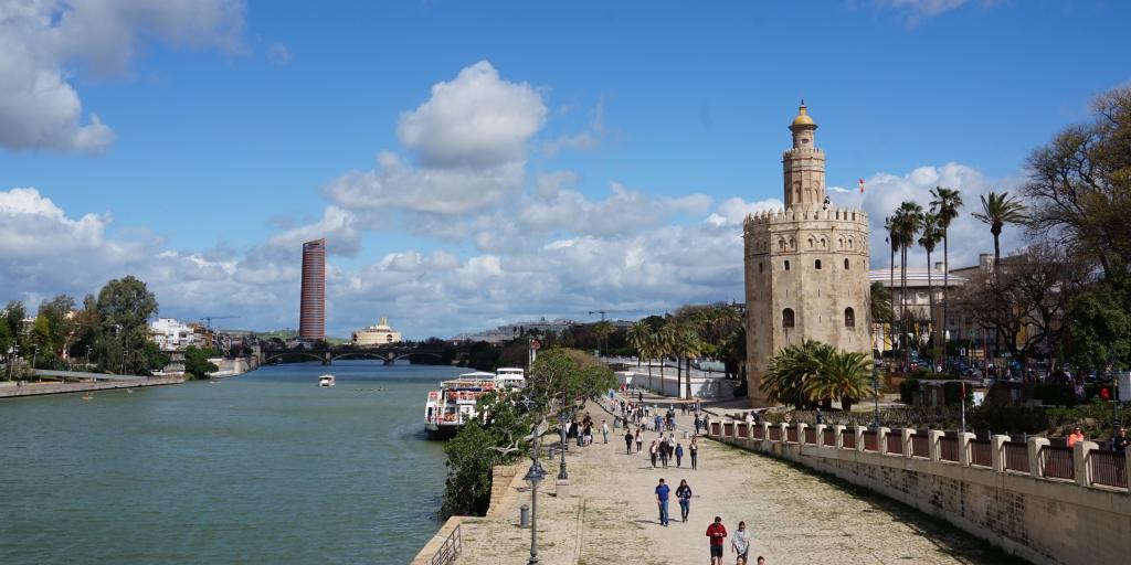 People walk along the banks of the Guadalquivir river in Seville, next to the Torre del Oro