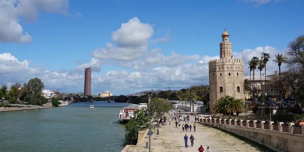 People walk along the banks of the Guadalquivir river in Seville, next to the Torre del Oro