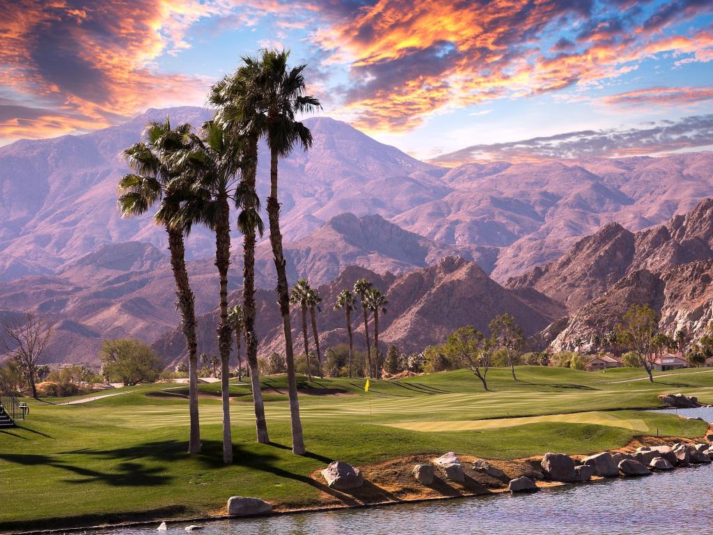 Palm Springs with a golf course and lake in the foreground, palm trees and mountains in the background.