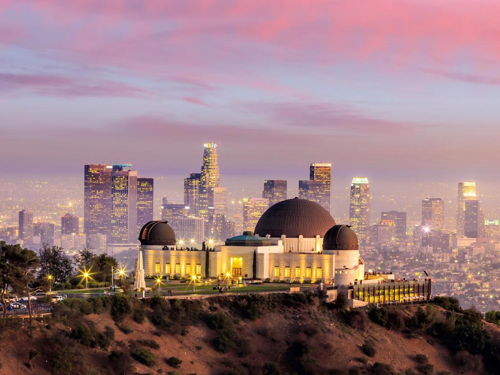 Griffith Observatory lit up at sunset with view of sky scrapers in the distance