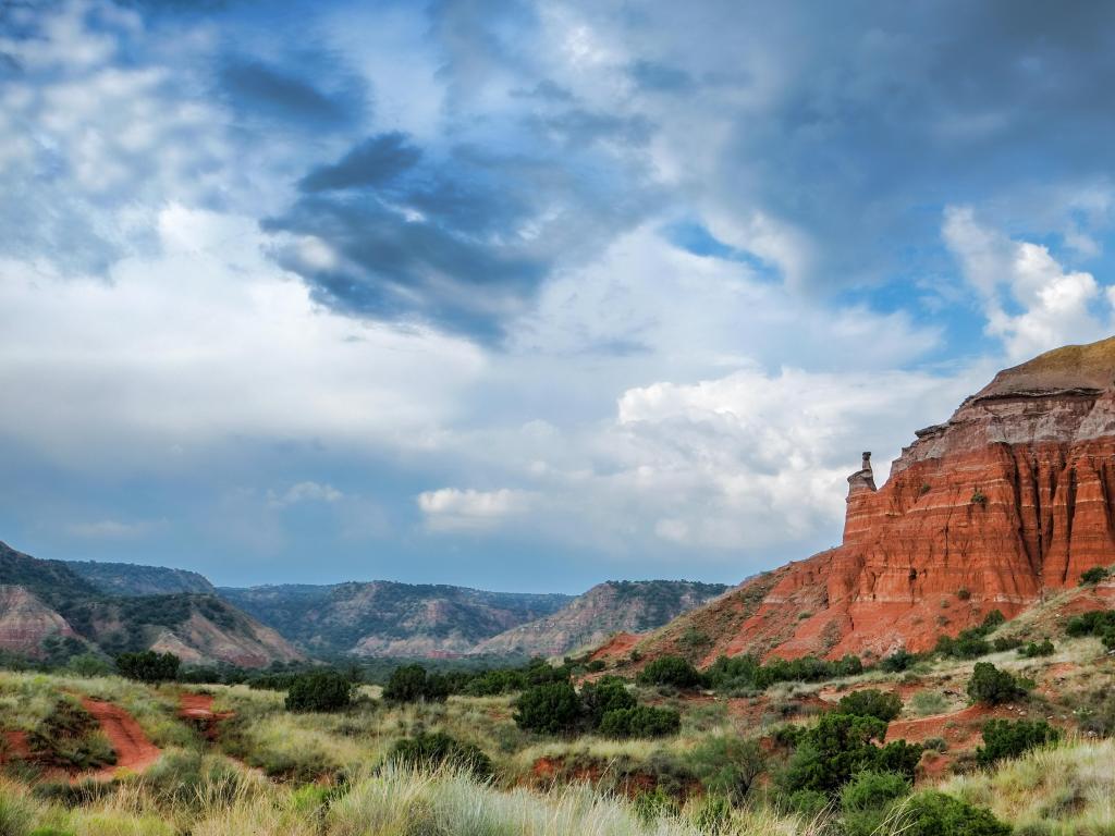 Palo Duro Canyon State Park, Texas with rock formations in the distance and green grasses in the foreground on a cloudy day.