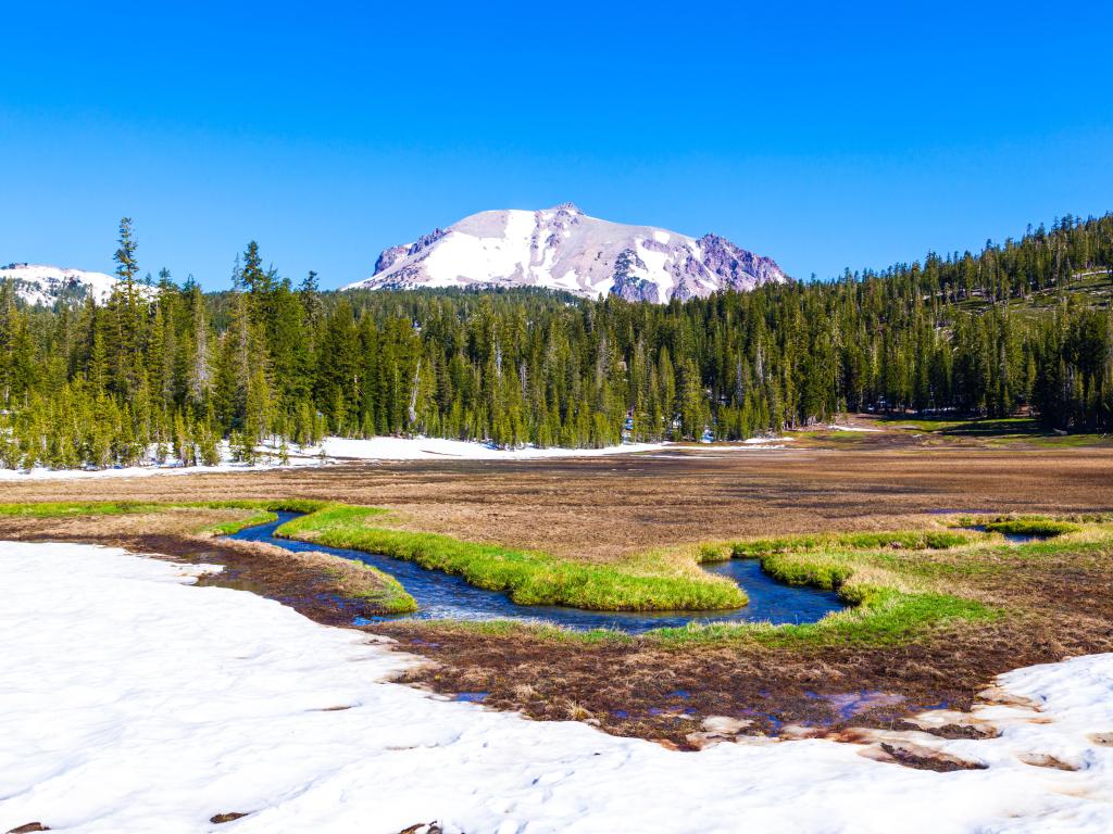 Lassen Volcanic National Park, California, USA with snow on Mount Lassen, a river and forest in the foreground taken on a sunny day.