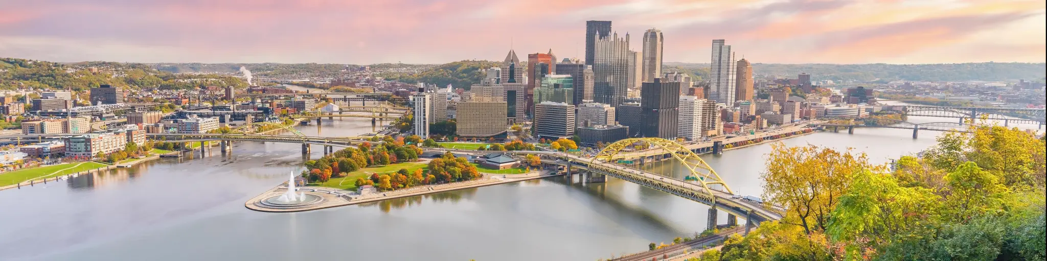 Pittsburgh, Pennsylvania at sunset with a view of a red mountain cart leading down to the city in the horizon and the river running through downtown.