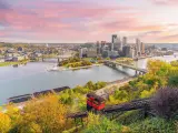 Pittsburgh, Pennsylvania at sunset with a view of a red mountain cart leading down to the city in the horizon and the river running through downtown.