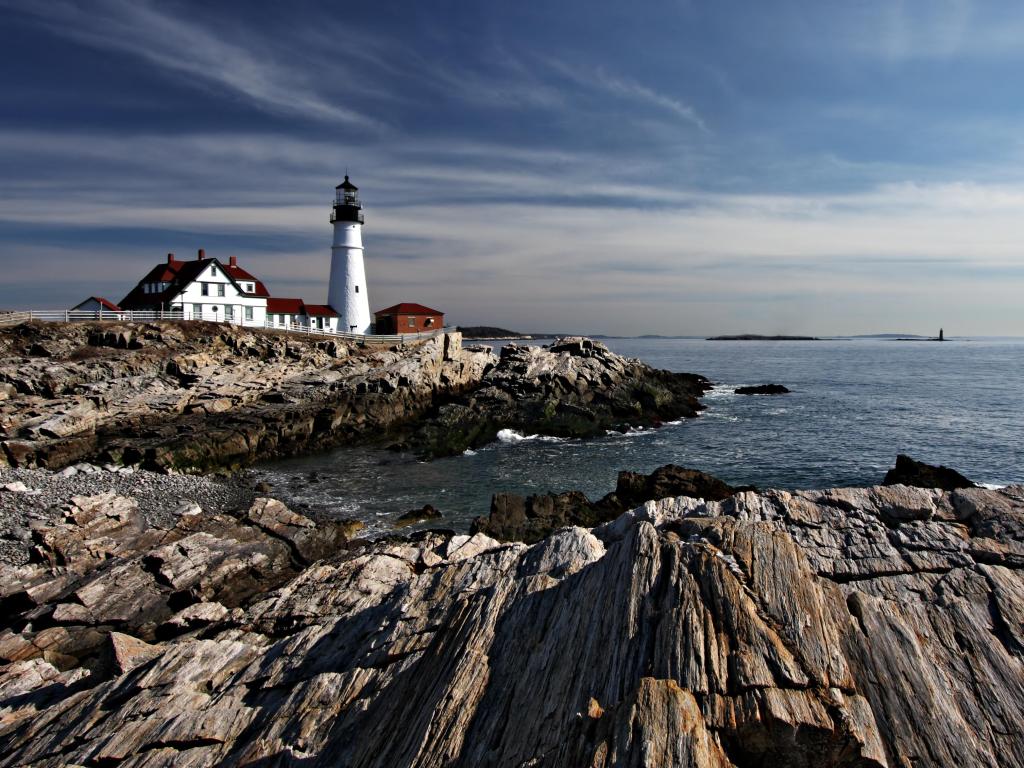 White lighthouse standing on low rocky cliffs with a grey sea and moody grey sky