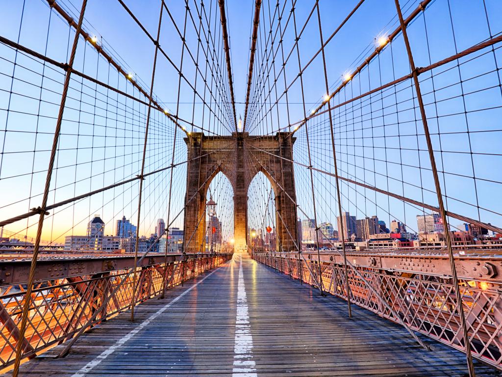 Empty Brooklyn Bridge in New York with buildings on the background and with lights on