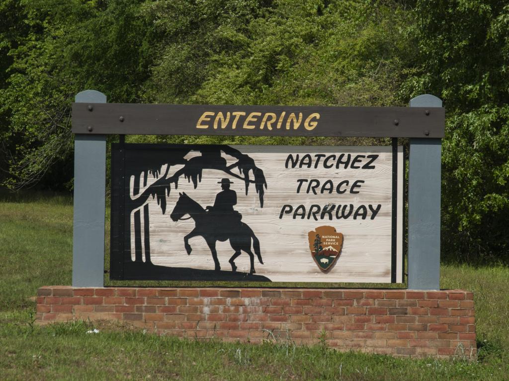 Sign at the entry to the Natchez Trace Parkway showing a man on horseback, with trees behind