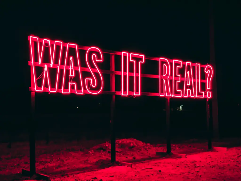 A red neon sign that says "Was it Real?" in Marfa, with a black background.