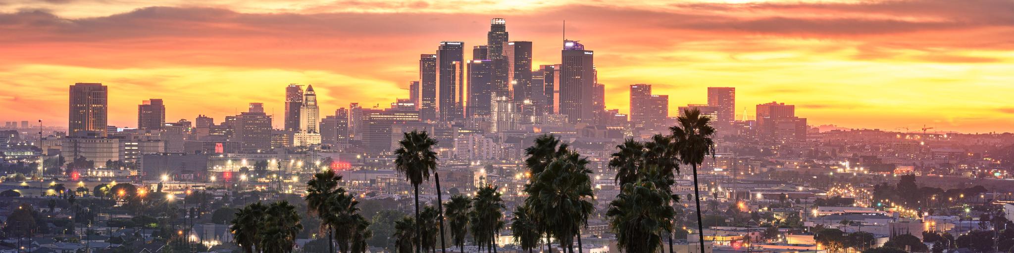Los Angeles, California, USA with the downtown skyline at sunset and palm trees in the foreground. 