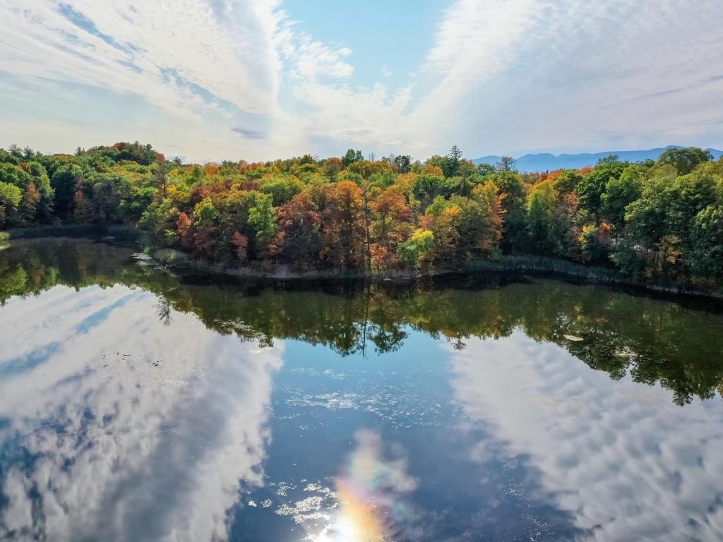 Olana State Historic Site in Hudson New York, Photo taken on a dramatically cloudy day, with the clouds reflecting on the water, surrounded by fall foliage trees