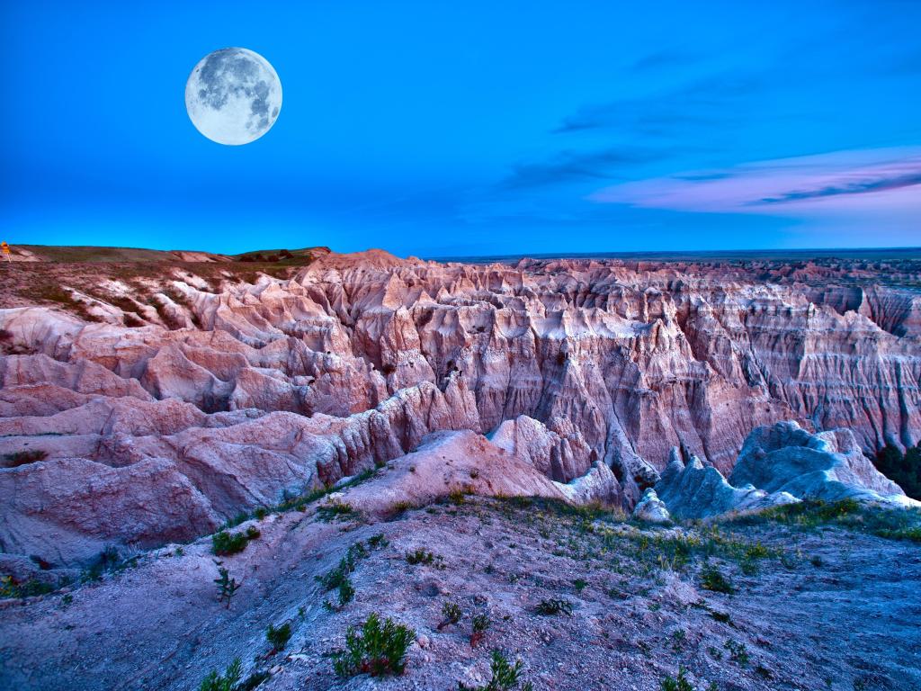 Badlands National Park at dusk with a full moon casting light over the jagged terrain