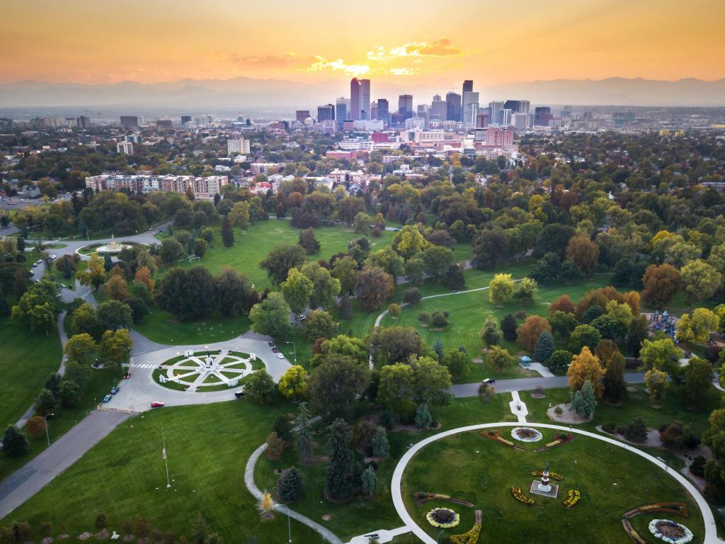 Denver skyline at dusk in the distance, the sky in orange tones, green park land in the foreground